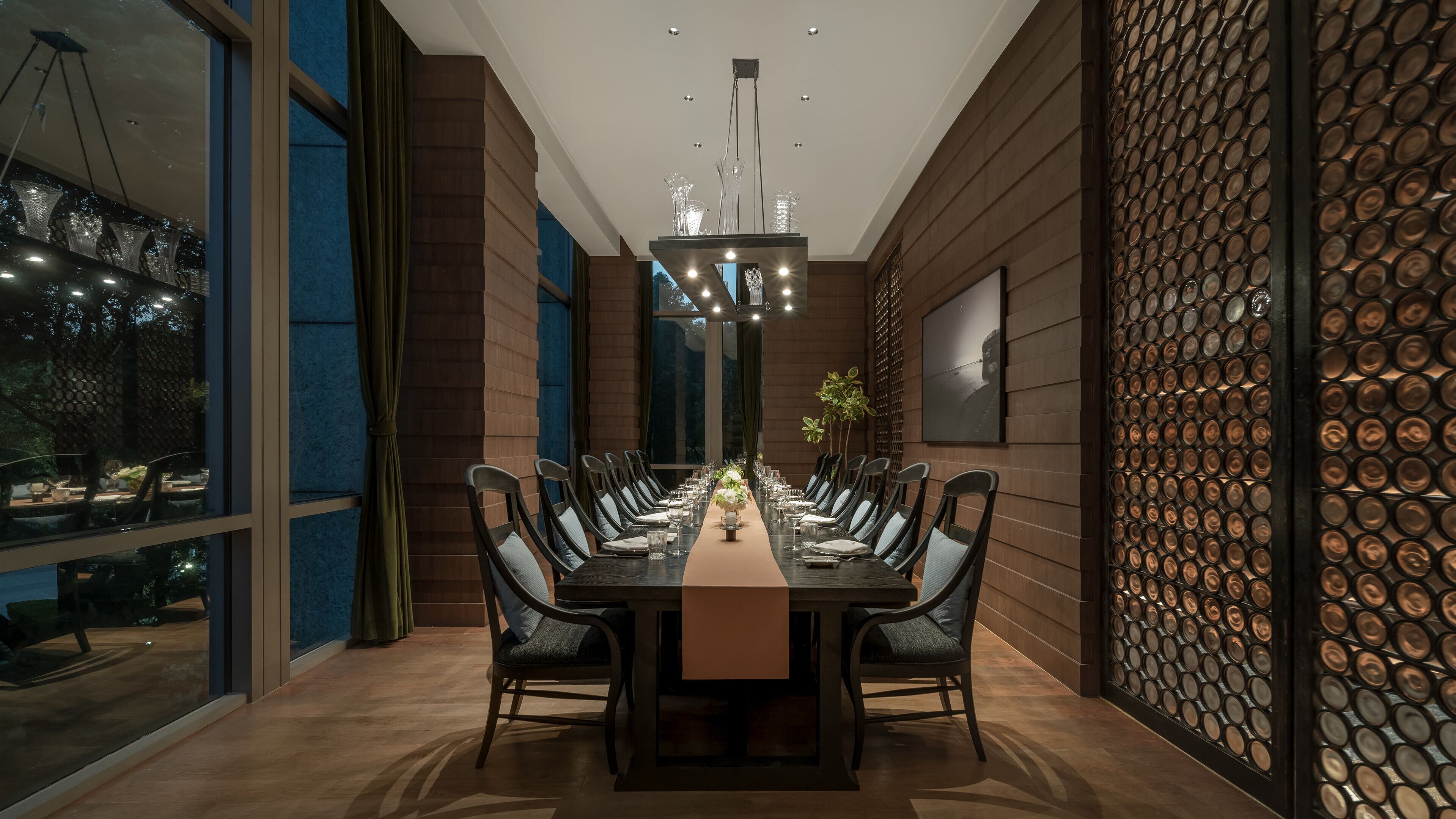 A modern dining area with a long table, chairs, and a chandelier.