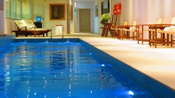 Una piscina con sillas de descanso y mesas, rodeada por un espacio interior bien iluminado con diseño moderno.