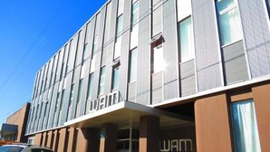 Un edificio moderno con un llamativo letrero 'WAM', que presenta una fachada limpia y estructurada con grandes ventanales y un techo plano.