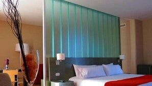 Una habitación de hotel moderna con una cama grande, una mesita de noche, una mesa de vidrio y un florero decorativo.