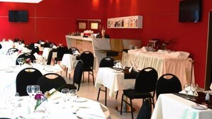 Comedor con mesas redondas dispuestas para varios comensales, con manteles blancos y sillas negras.