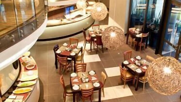 A modern restaurant with a curved layout, multiple dining tables, and hanging spherical light fixtures. - Peermont Metcourt Hotel at Umfolozi (Empangeni)