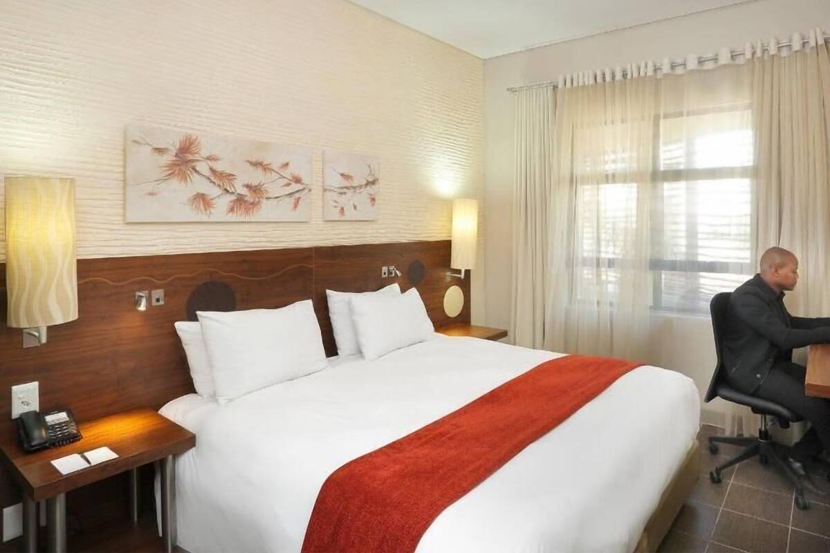 A hotel room with a large bed, a desk, a lamp, and artwork on the wall.