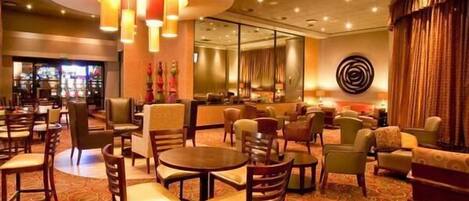 Un hall d’hôtel avec des tables rondes, des chaises et un coin bar.