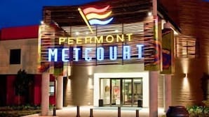 A hotel entrance with a neon sign reading "PEERMONT METROURT" and a flag above it. - Peermont Metcourt Hotel at Umfolozi (Empangeni)