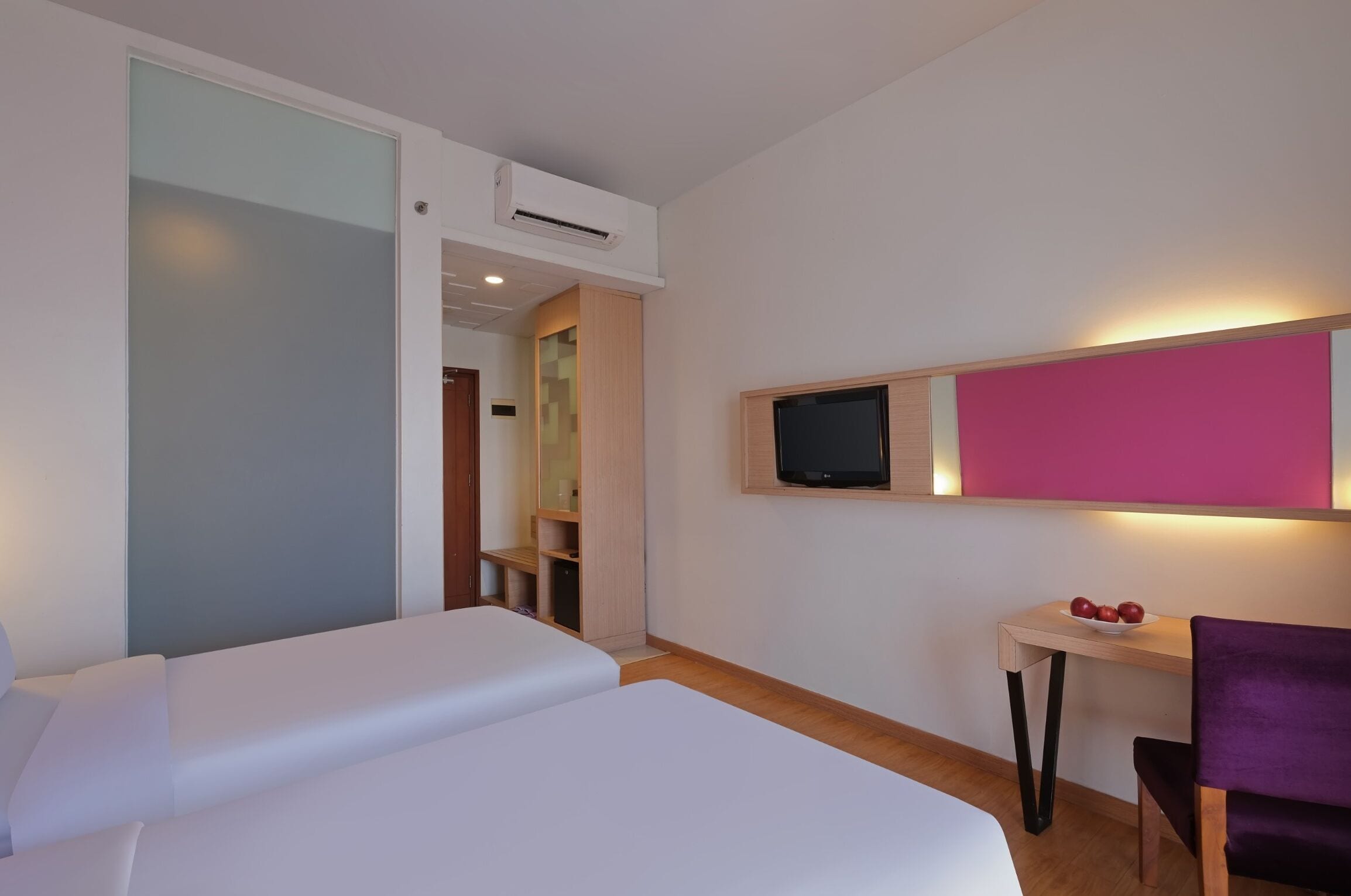 Une chambre d’hôtel avec deux lits, un bureau avec un ordinateur, une télévision et une petite table avec des fruits.