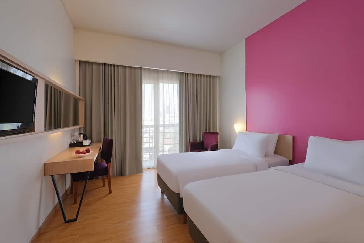 Ein Hotelzimmer mit zwei Betten, einem Schreibtisch mit Stuhl, einem Fernseher und einem Fenster mit Vorhängen.