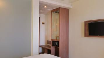 A hotel room with a bed, a wooden wardrobe, a television mounted on the wall, and a bench.
