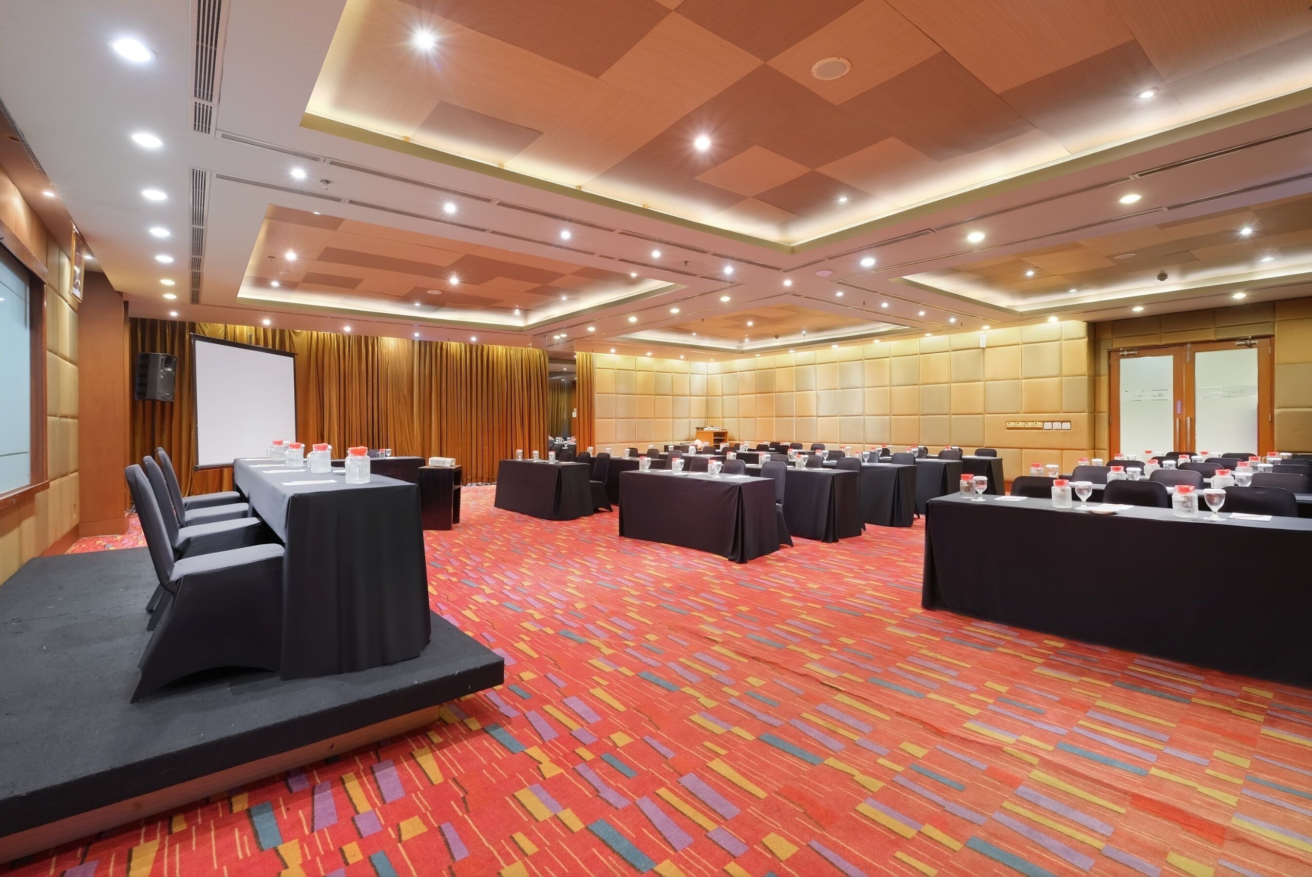 Un salón de conferencias con varias mesas, sillas y un escenario.