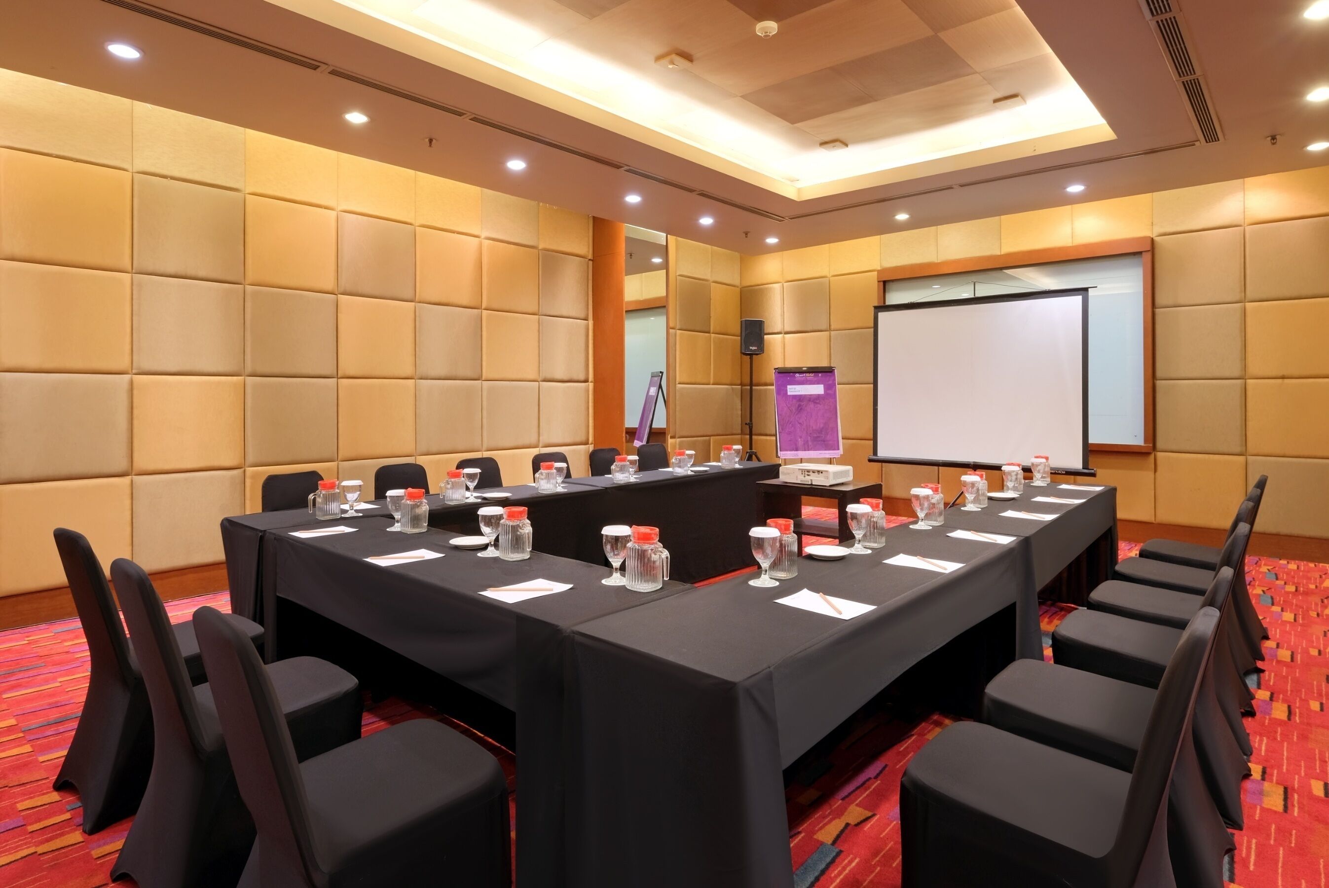 Un salón de conferencias con una larga mesa, sillas y una pantalla de proyector.