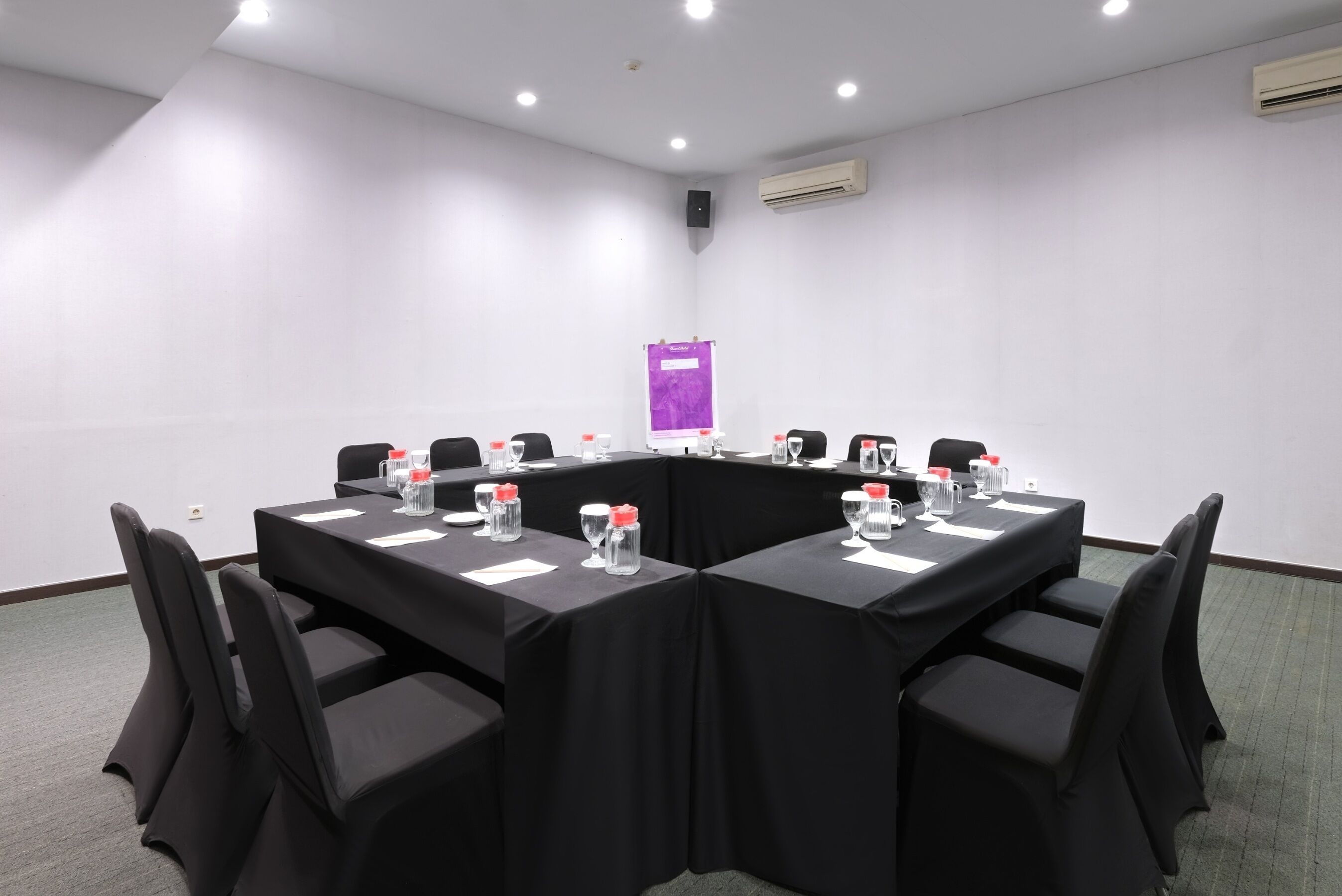 A conference room with a long table, black chairs, and a purple banner on the wall.