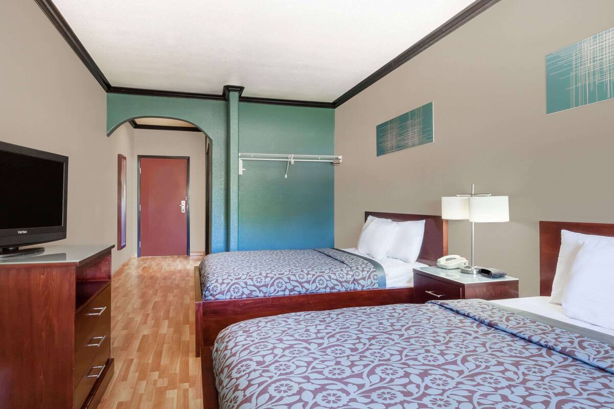 A hotel room with two beds, a TV, a desk, and a door leading to another room.
