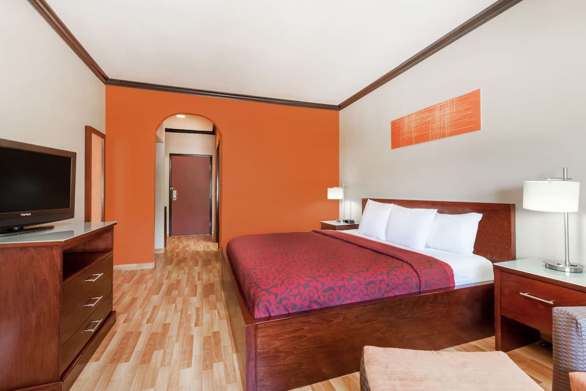 A hotel room with a wooden bed, a TV, a desk, and a lamp.