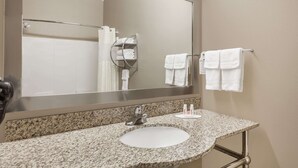 Un baño con encimera de granito, un lavamanos blanco, un espejo grande y un toallero con dos toallas.