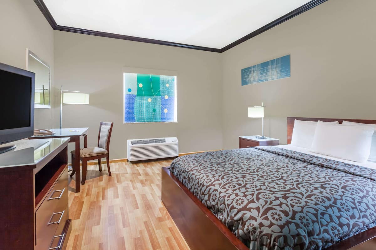 A hotel room with a bed, a desk with a TV, a chair, a window with a view, and an air conditioning unit.