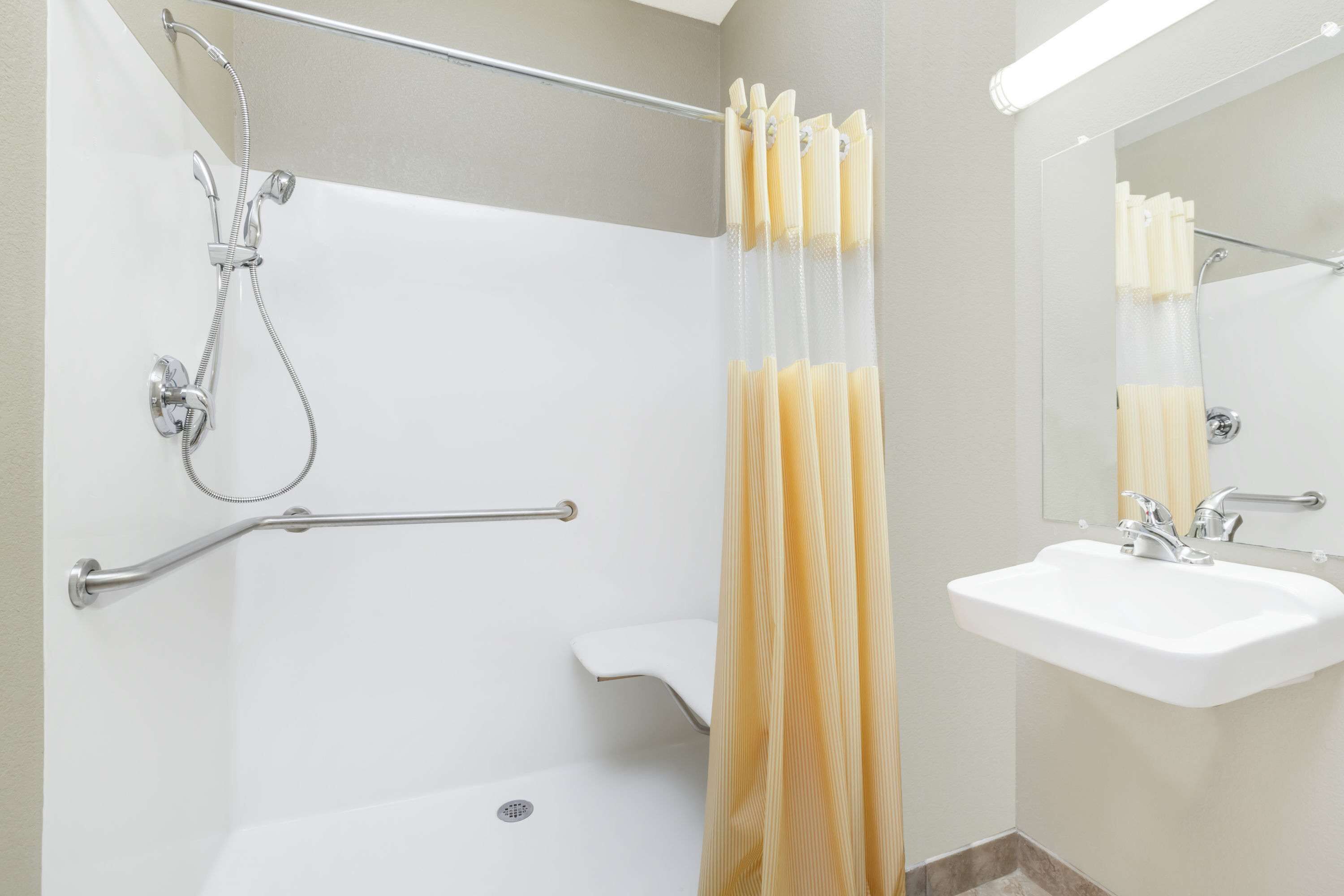 A bathroom with a bathtub, a shower, a handrail, a sink, and a mirror.