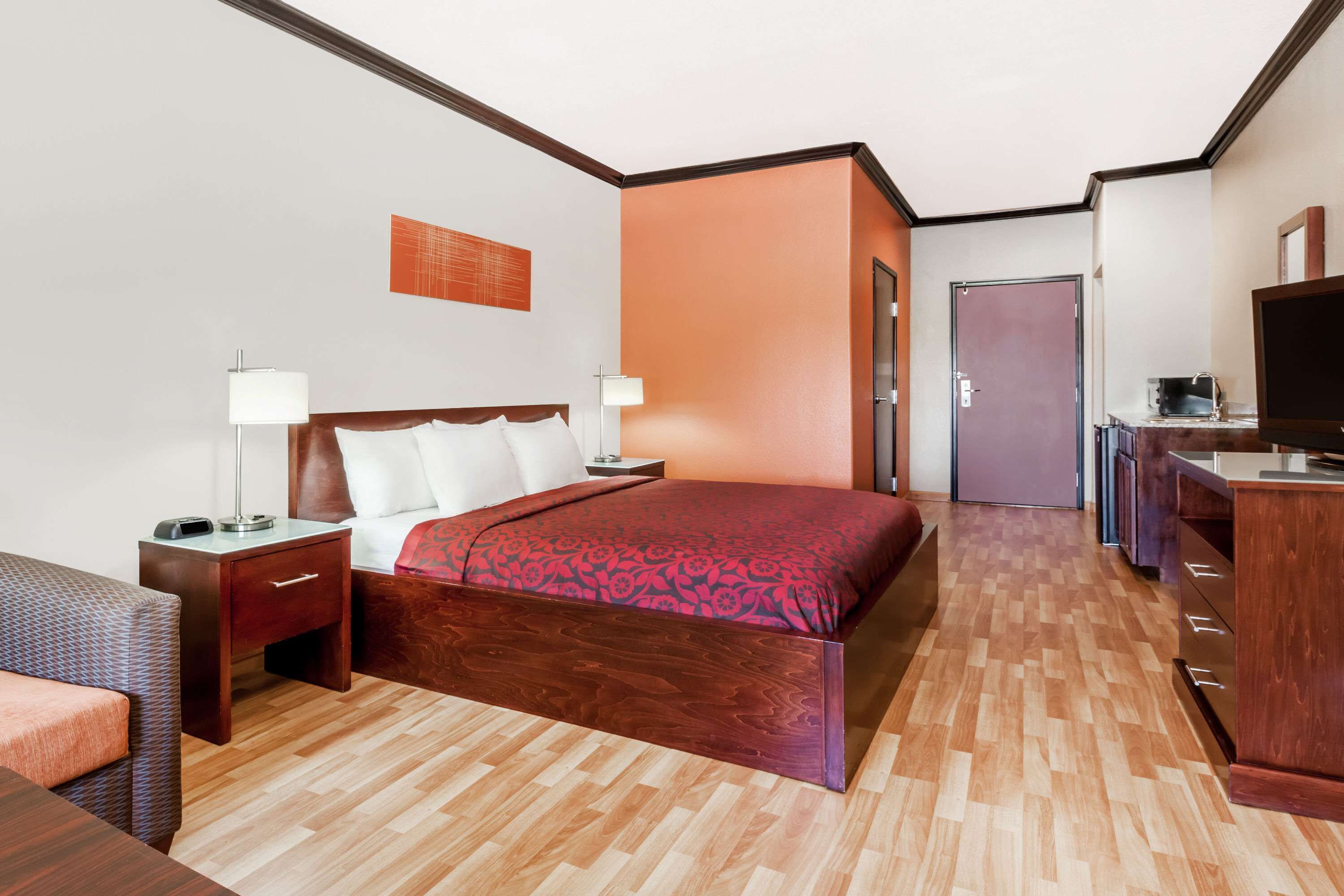 Een hotelkamer met een houten bed, twee nachtkastjes met lampen, een flatscreen televisie, een houten dressoir en een deur naar een andere kamer.