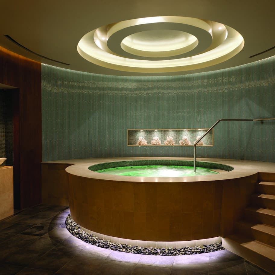 A modern spa area with a circular hot tub, a staircase, and a wall with a textured pattern.