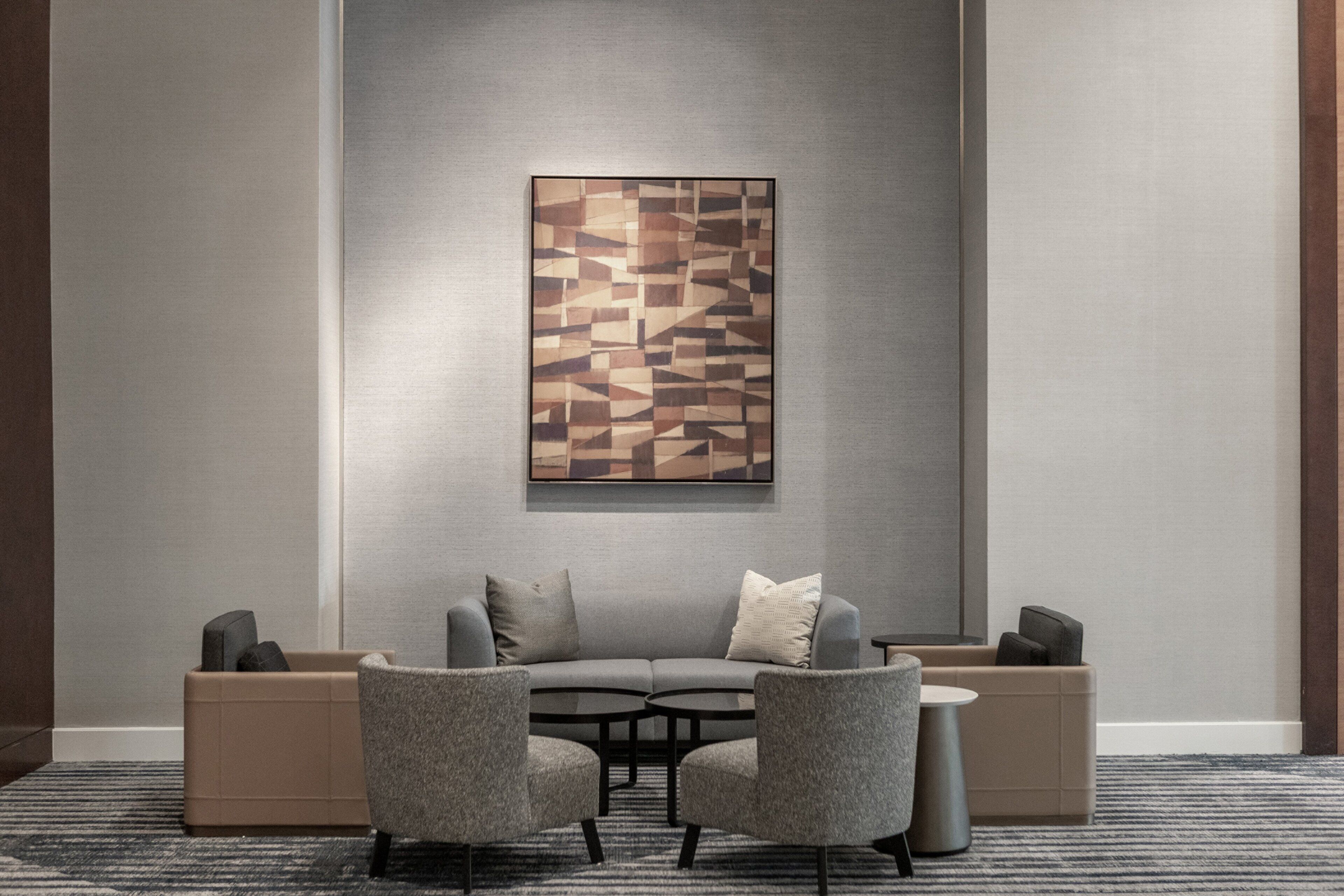 Un espace de détente moderne comprenant un canapé gris, deux fauteuils, une petite table ronde et une œuvre d’art murale aux motifs géométriques.
