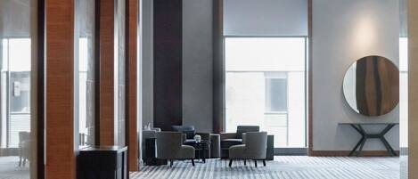 Un hall d’hôtel moderne avec une grande fenêtre, un grand miroir rond et un espace salon comprenant une petite table et des chaises.