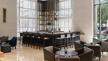 Een moderne bar met een centraal eiland, barstoelen en een zithoek met ronde tafels en stoelen.