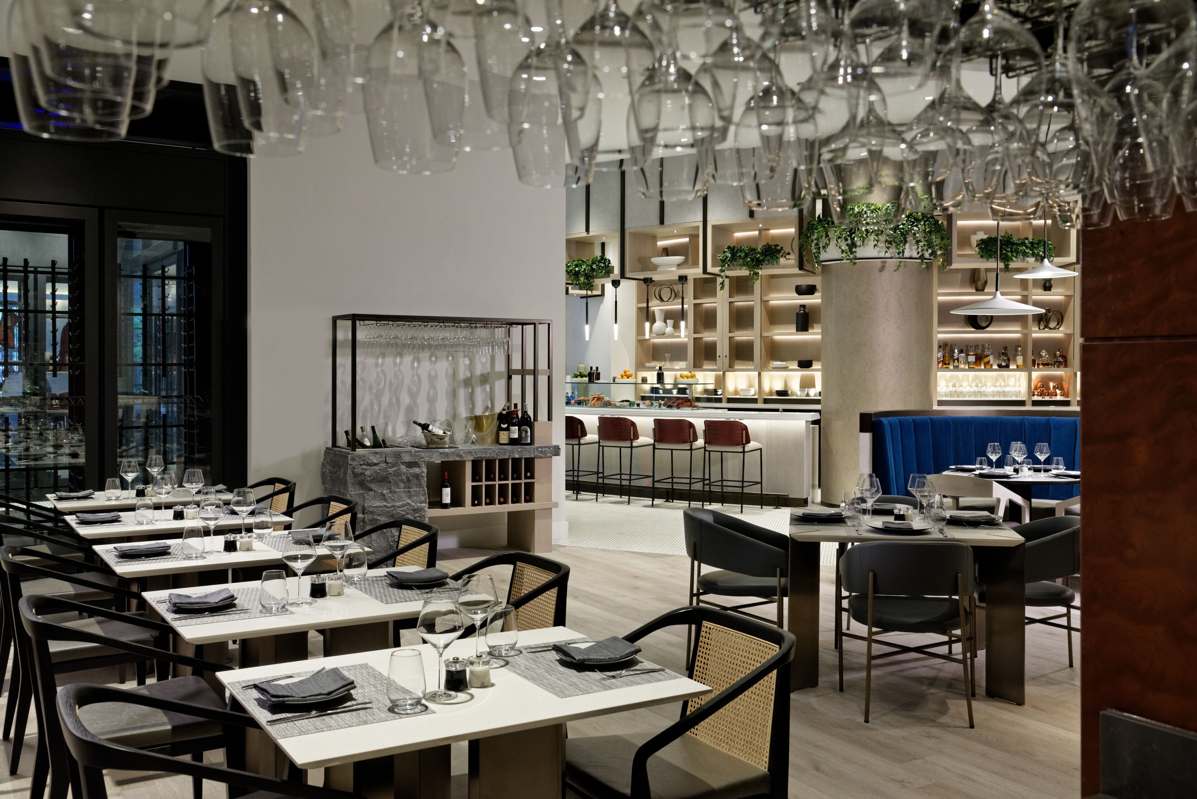Un restaurante moderno con varias mesas y sillas, una zona de bar y un techo decorativo con copas colgantes.