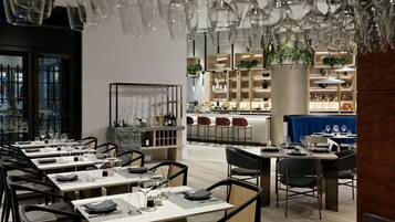 Un restaurante moderno con varias mesas y sillas, una zona de bar y un techo decorativo con copas colgantes.