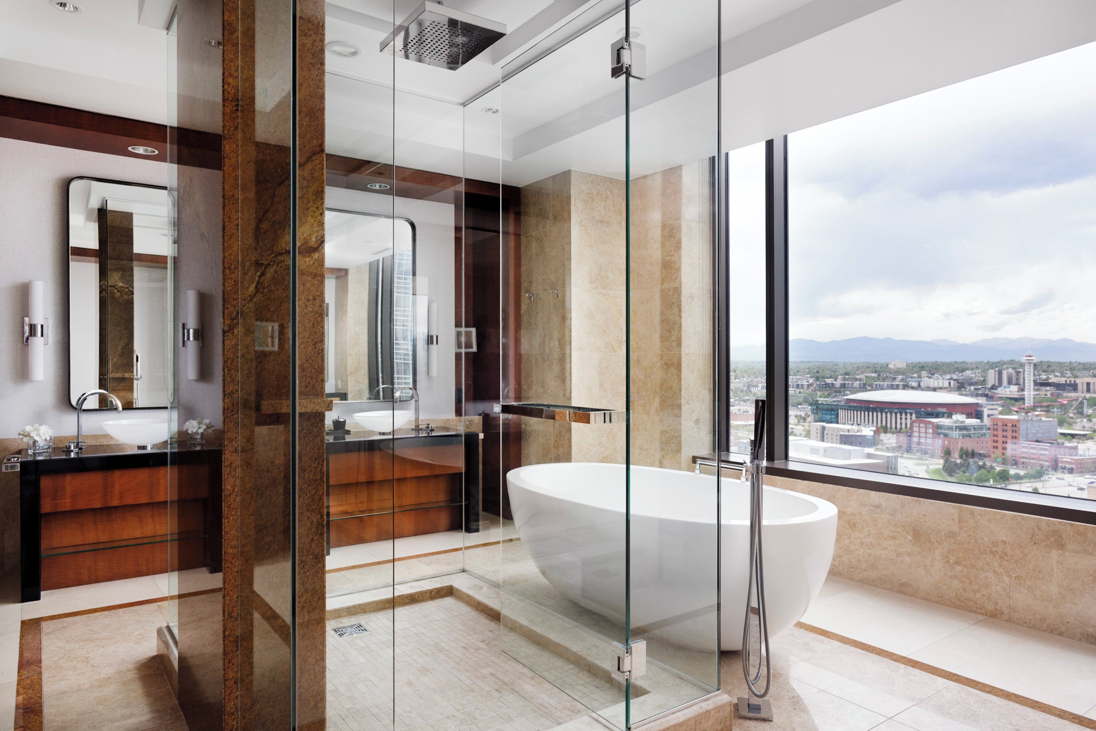 A modern bathroom with a large bathtub, a glass-enclosed shower, and a city view.