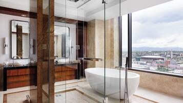 A modern bathroom with a large bathtub, a glass-enclosed shower, and a city view.