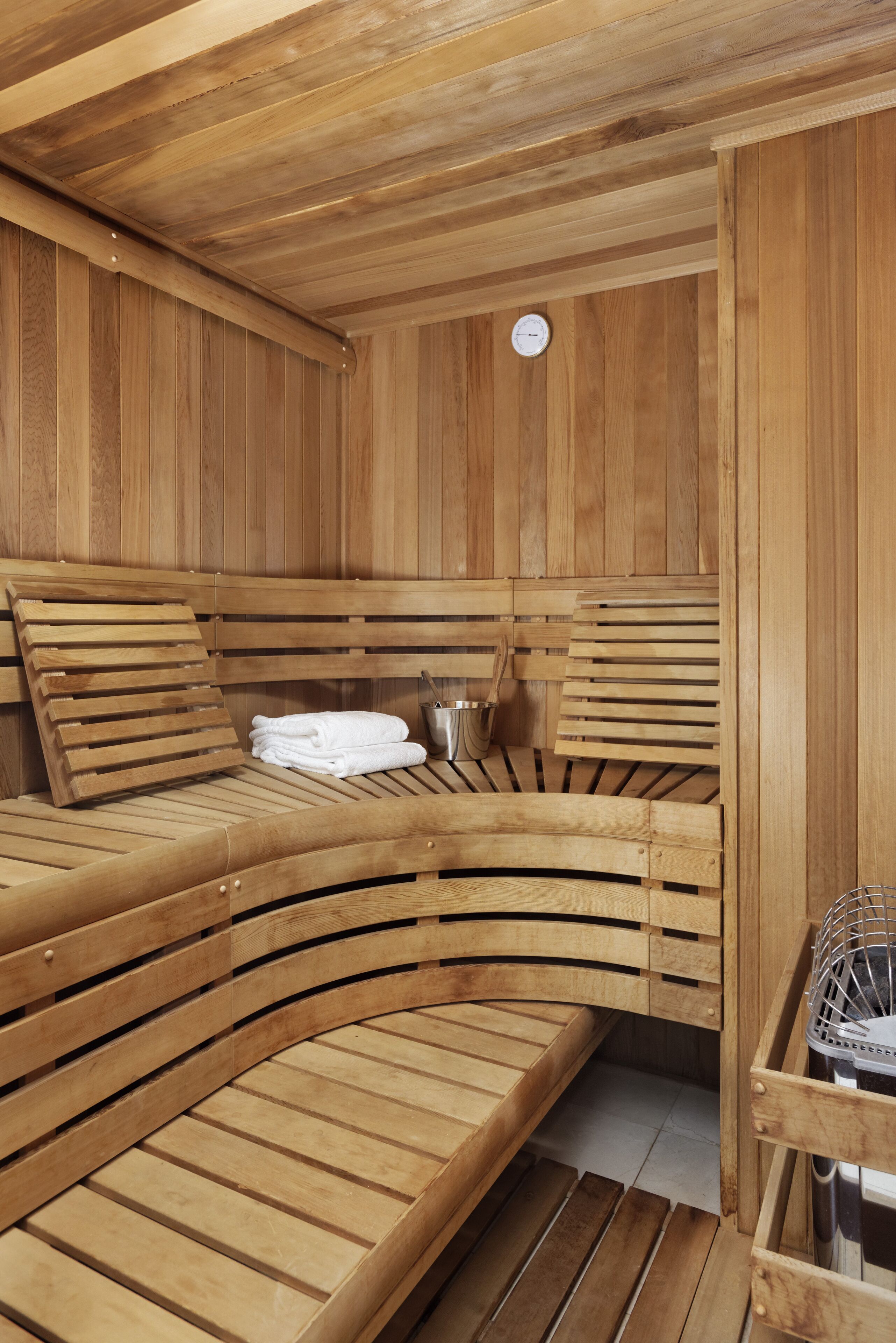 A wooden sauna with benches and a bench seat, a clock, and a metal container.
