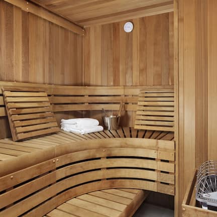 A wooden sauna with benches and a bench seat, a clock, and a metal container.