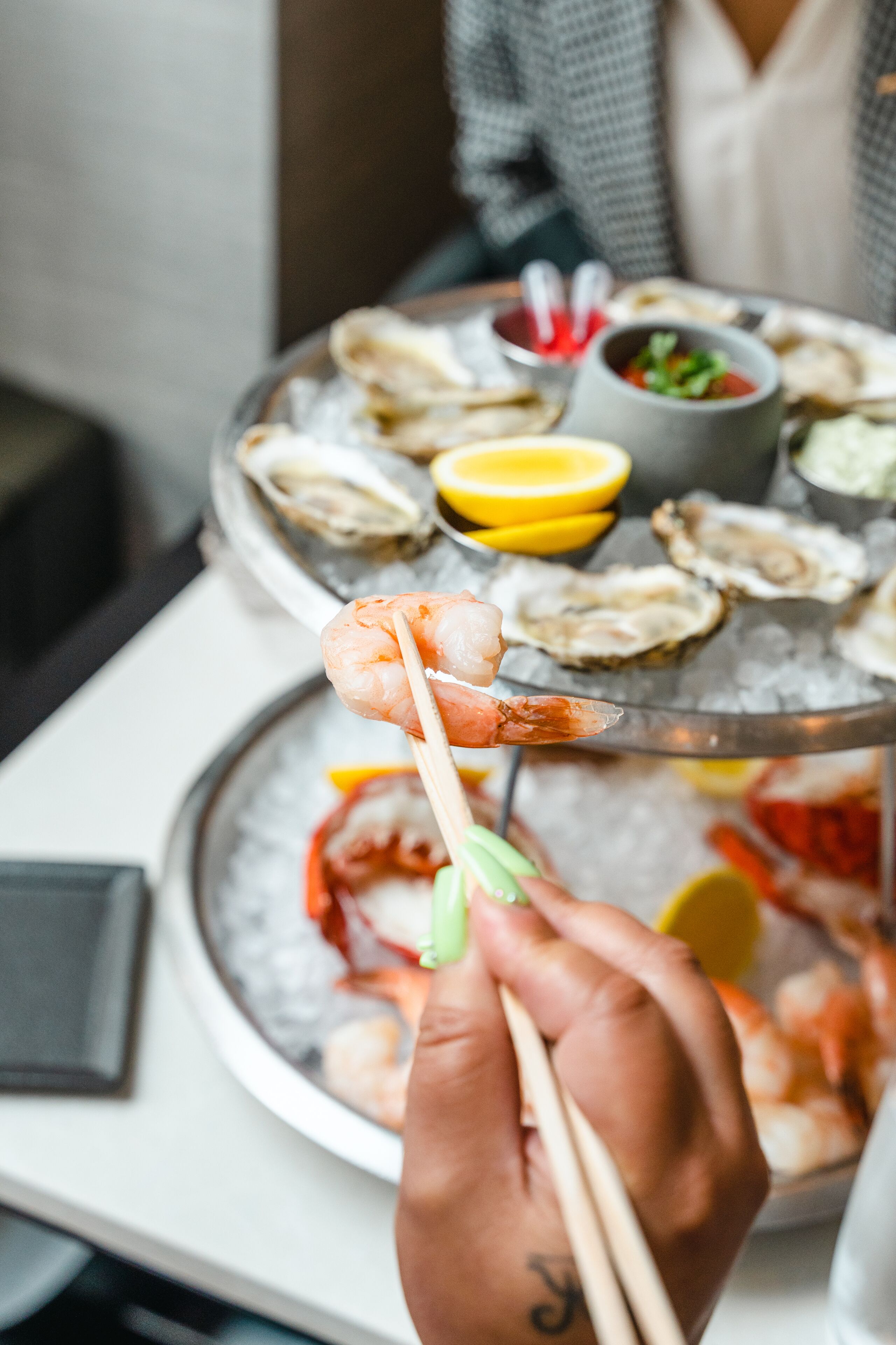 A seafood platter with shrimp and oysters on ice, accompanied by lemon wedges and dipping sauces.