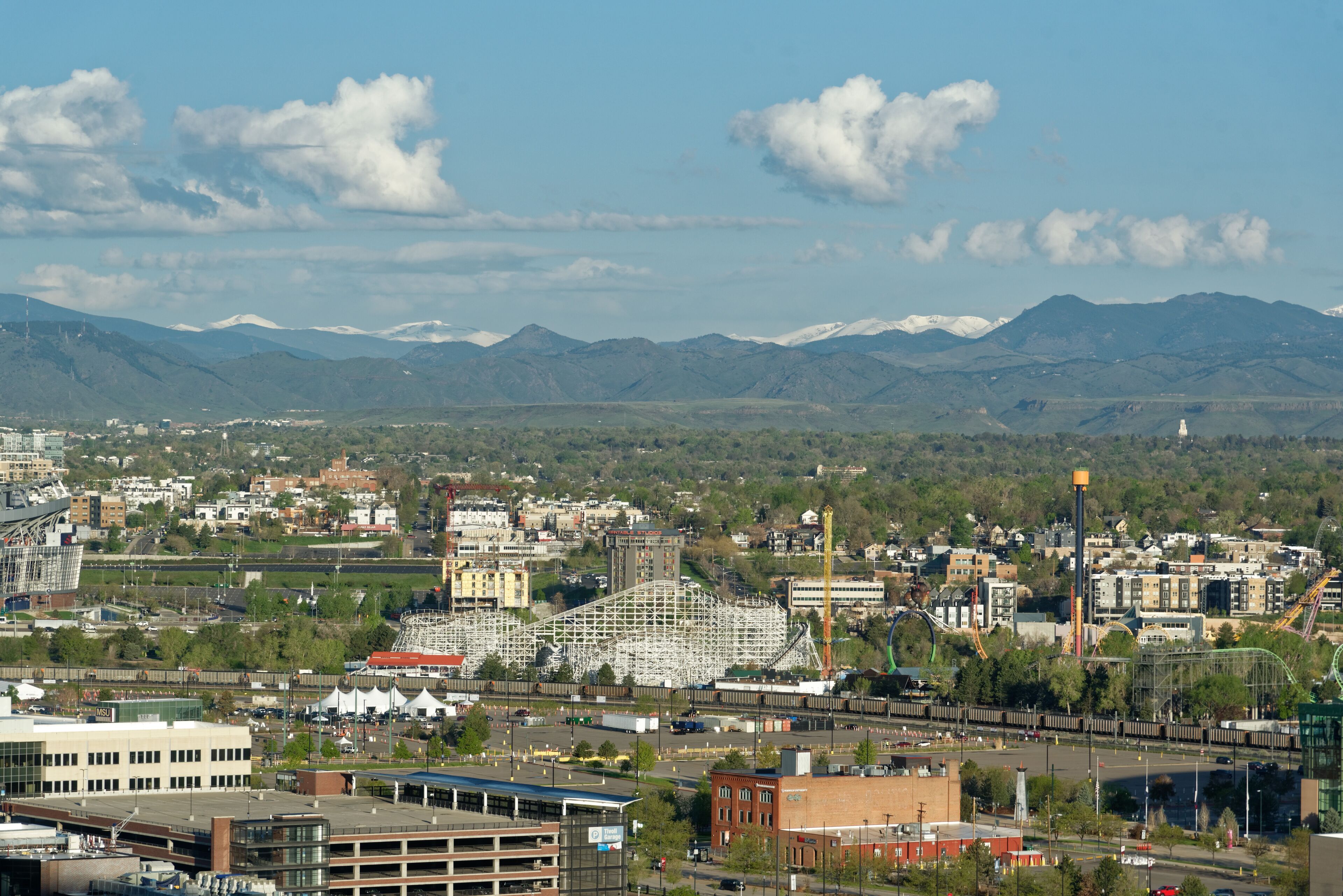 A cityscape with a roller coaster, buildings, and mountains in the background.