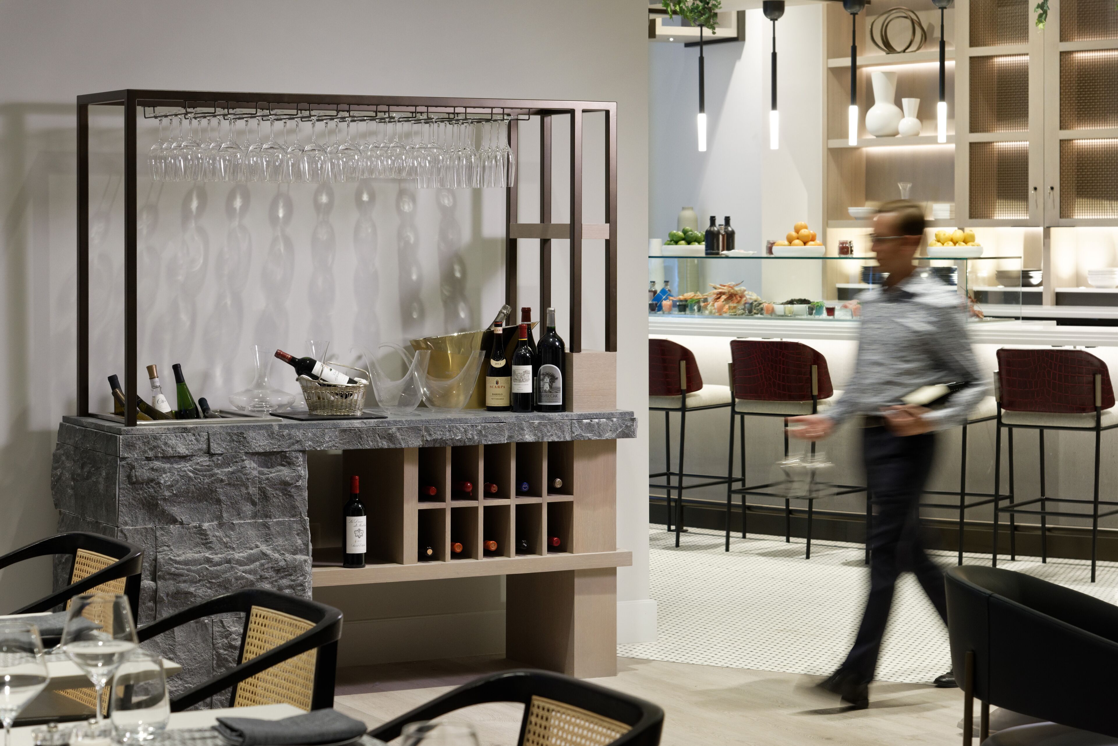 A modern bar area with wine bottles, glasses, and a seating arrangement.