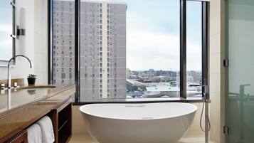A modern bathroom with a freestanding bathtub, a large window with a city view, and a vanity with a mirror and sink.