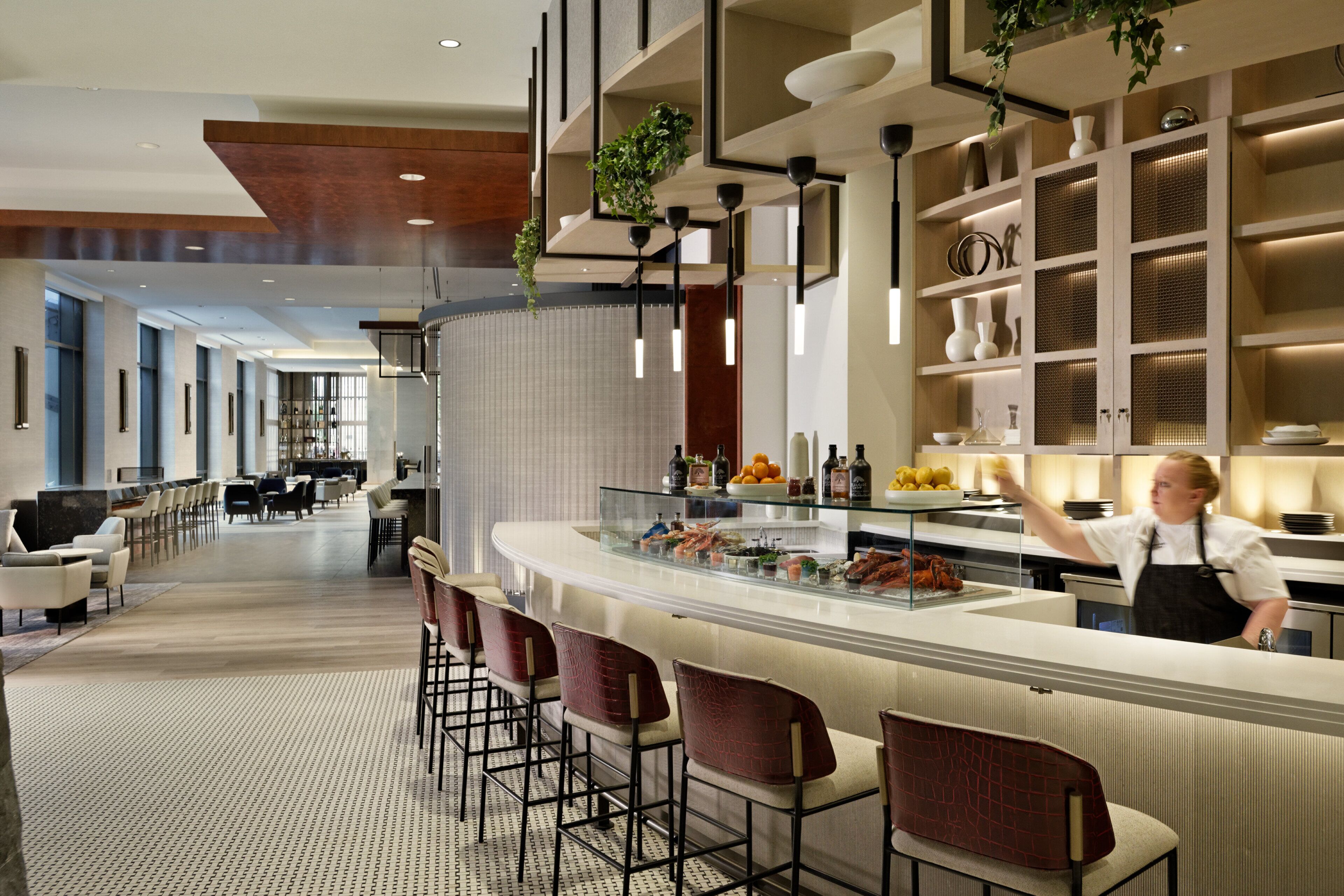 A modern bar area with a counter, bar stools, and a chef preparing food.