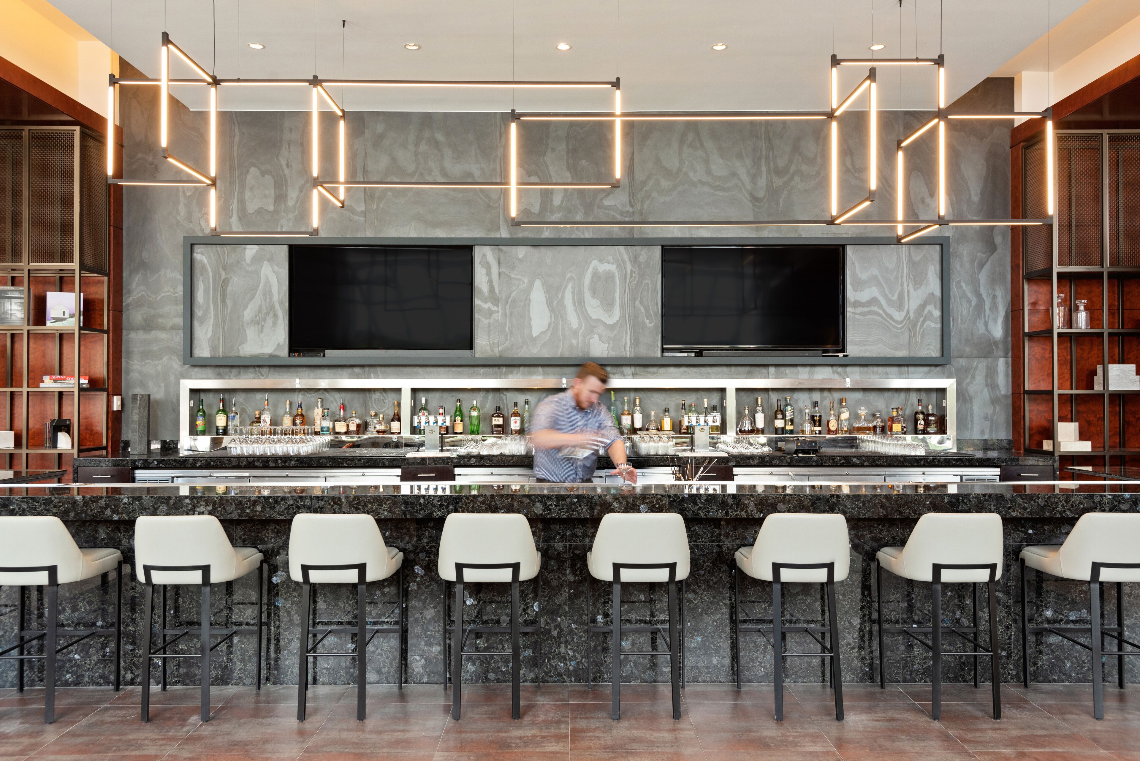 A bar area with a bartender, marble countertops, and bar stools.