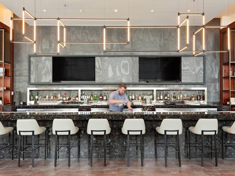 A bar area with a bartender, marble countertops, and bar stools.