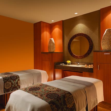 A hotel room with two beds, a bathroom with a mirror, and a vanity with a vase.
