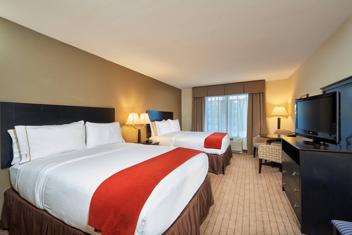 A hotel room with two beds, a TV, a desk, and a window with curtains.