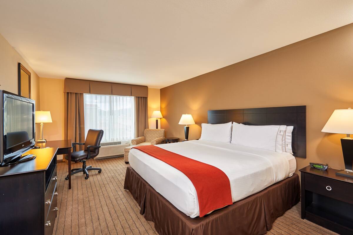 A hotel room with a large bed, a desk with a television, two chairs, and two bedside lamps.