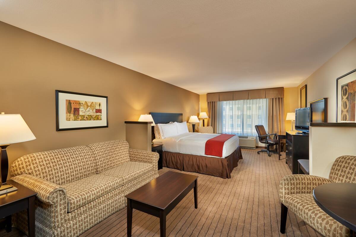 A hotel room with a bed, two sofas, a coffee table, a desk with a computer, and a TV.