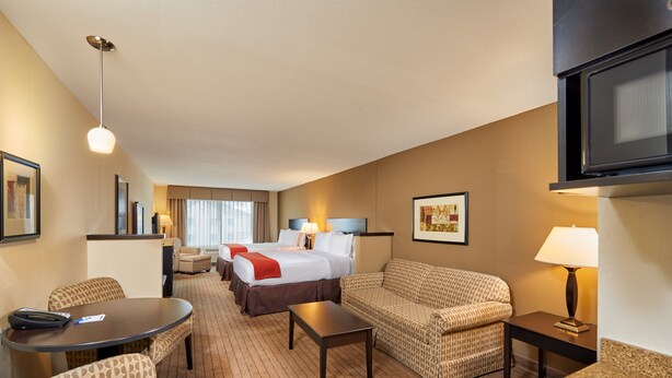 Quarto de hotel com cama, dois sofás, mesa de jantar, televisão e luminária.