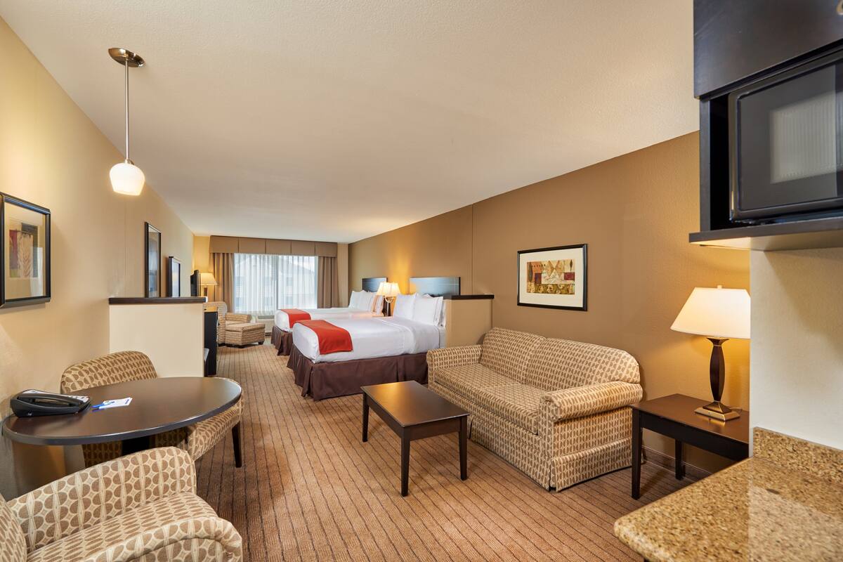 A hotel room with a bed, two sofas, a dining table, a TV, and a lamp.