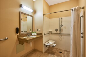 Un bagno con lavandino, specchio, porta asciugamani e doccia dotata di maniglie di sostegno.
