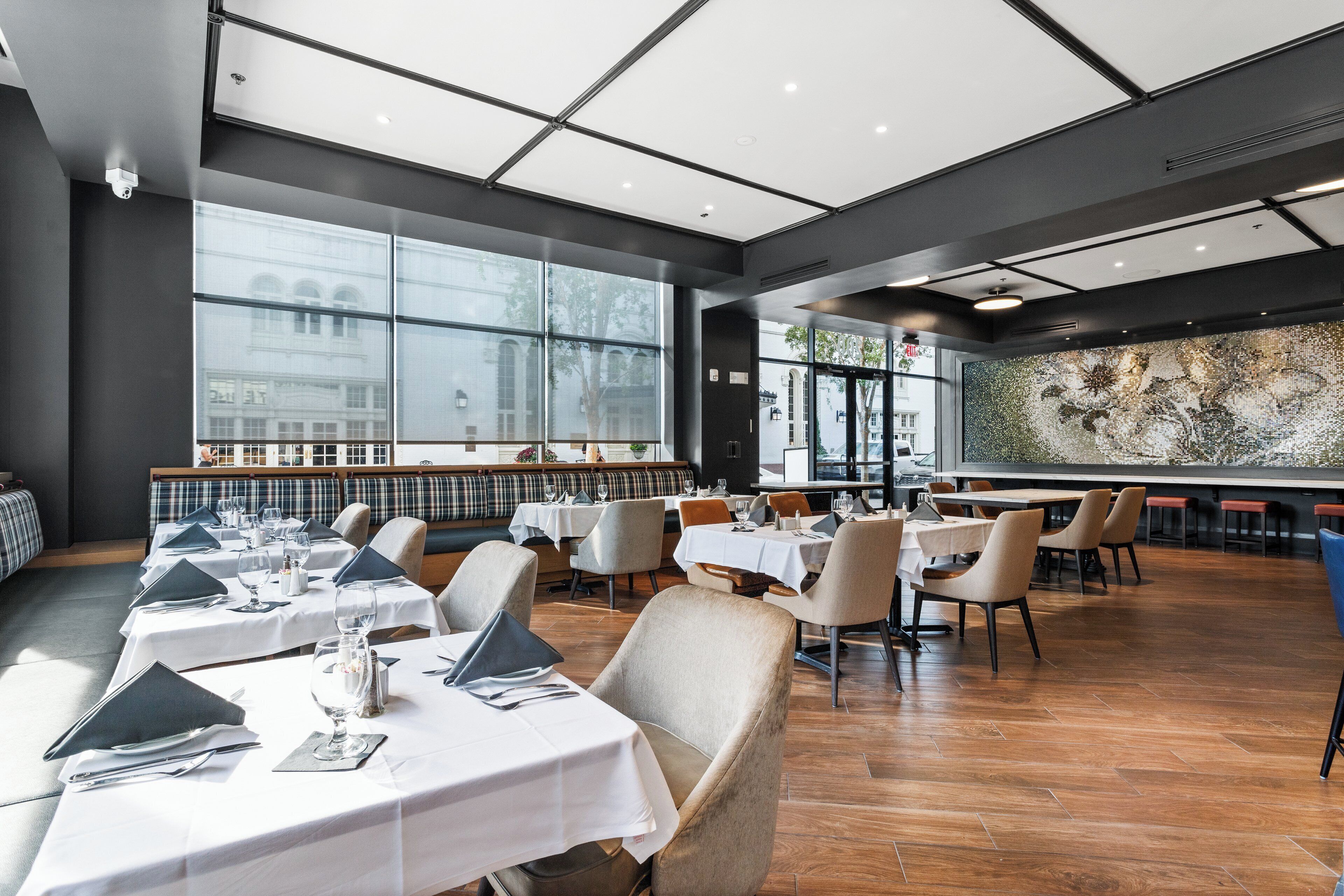 A modern restaurant with a long counter, multiple tables, and a large window offering a view of the city.