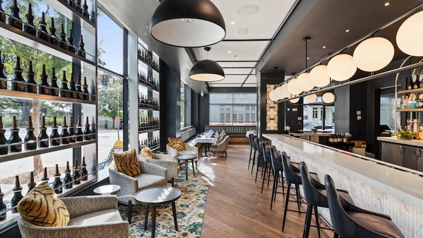 Uma área de bar moderna com prateleiras de garrafas, assentos e iluminação pendente.
