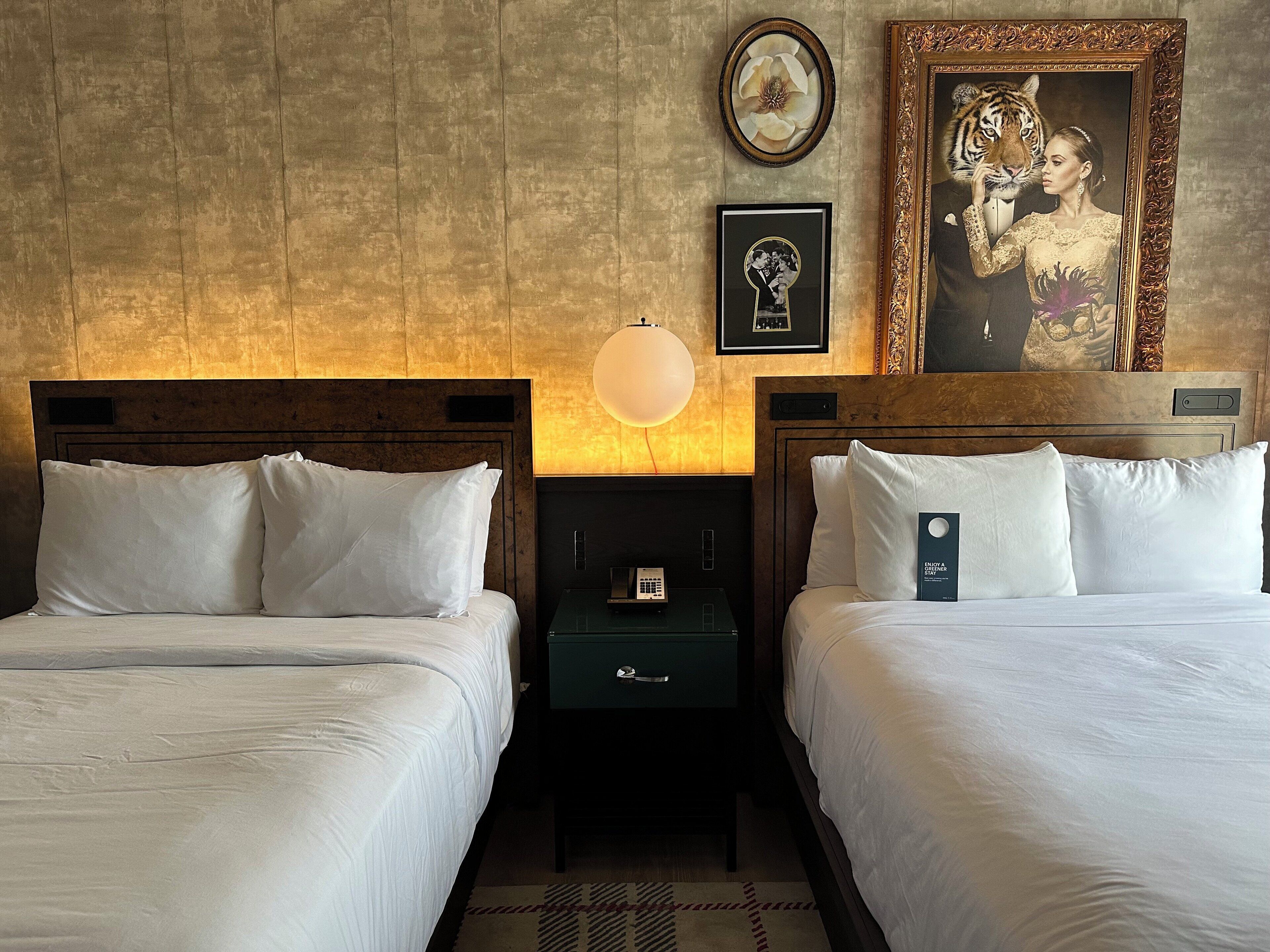 A hotel room with two beds, a nightstand, a lamp, and framed artwork on the wall.