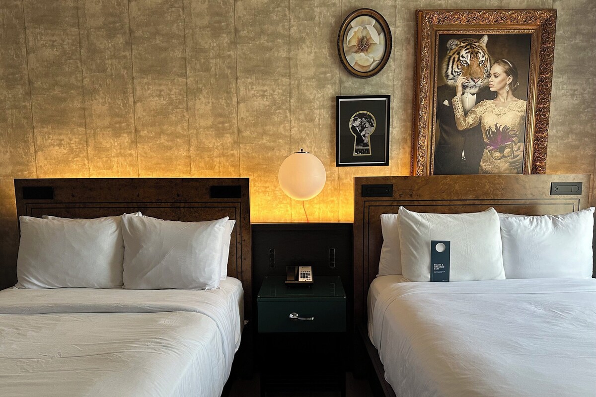 A hotel room with two beds, a nightstand with a lamp, and a framed picture on the wall.