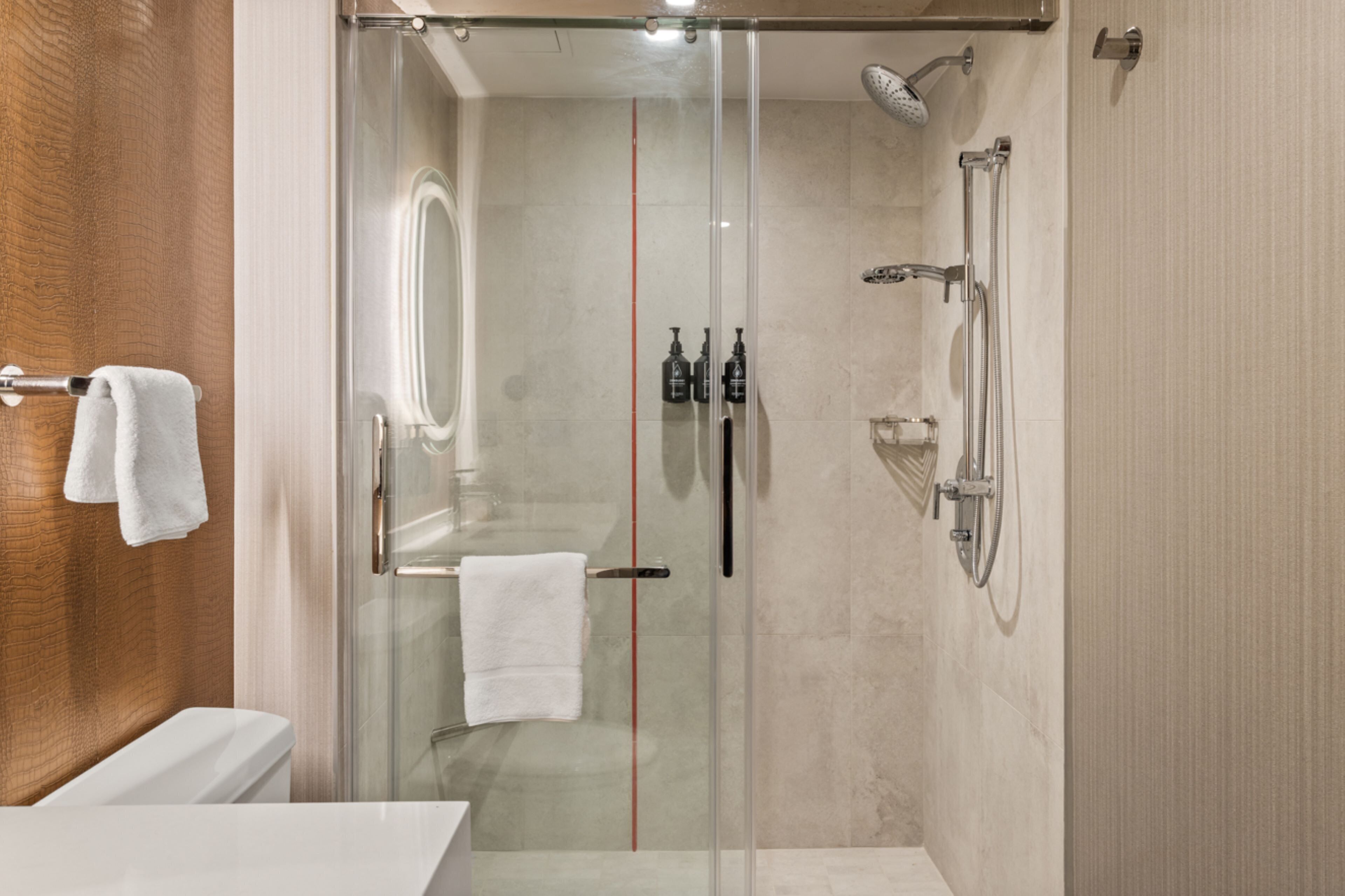 A modern bathroom with a glass-enclosed shower, a white toilet, and a wooden panel wall.